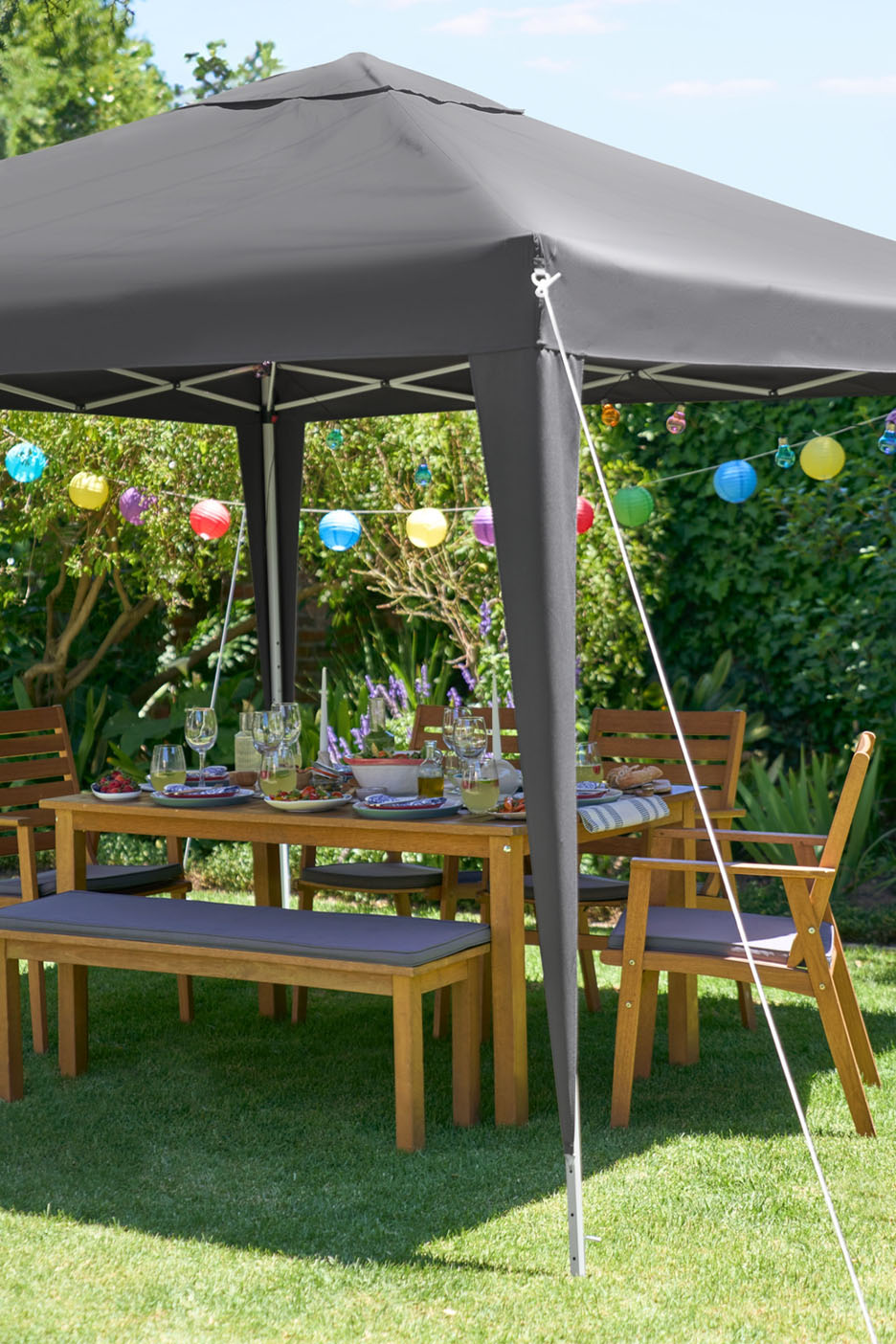 Un gazebo de jardin avec une table et des bancs en bois, décoré de lanternes colorées.