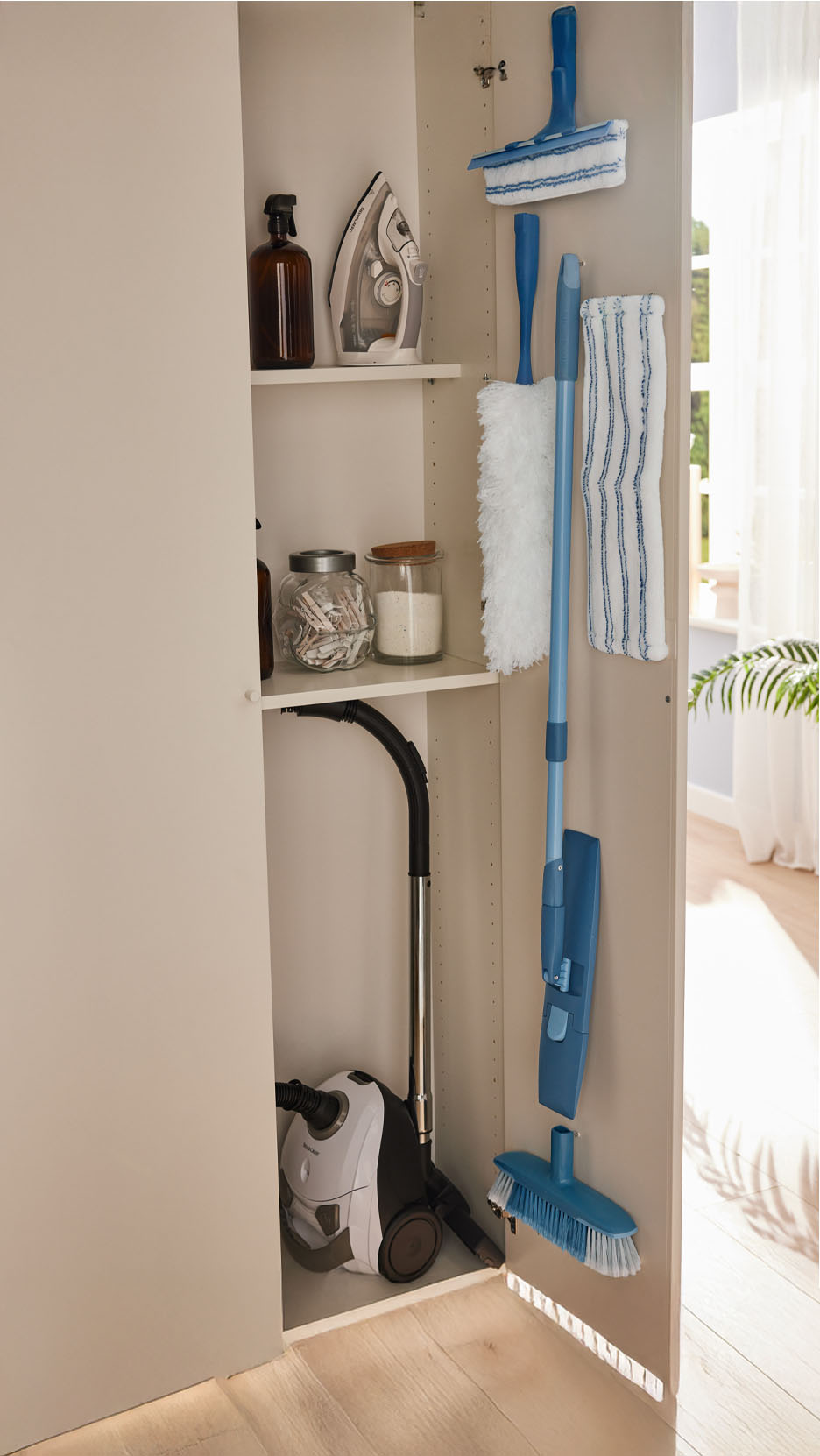Un placard de rangement bien organisé avec un aspirateur Thomas, un fer à repasser et des outils de nettoyage.