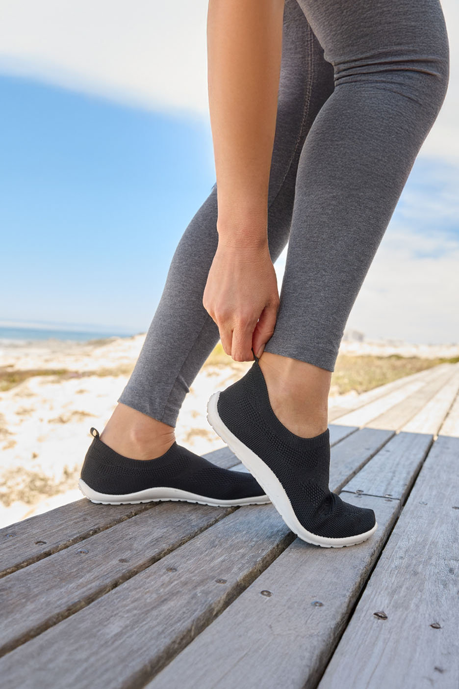 Une femme sur la plage enfile des baskets noires en tricot.