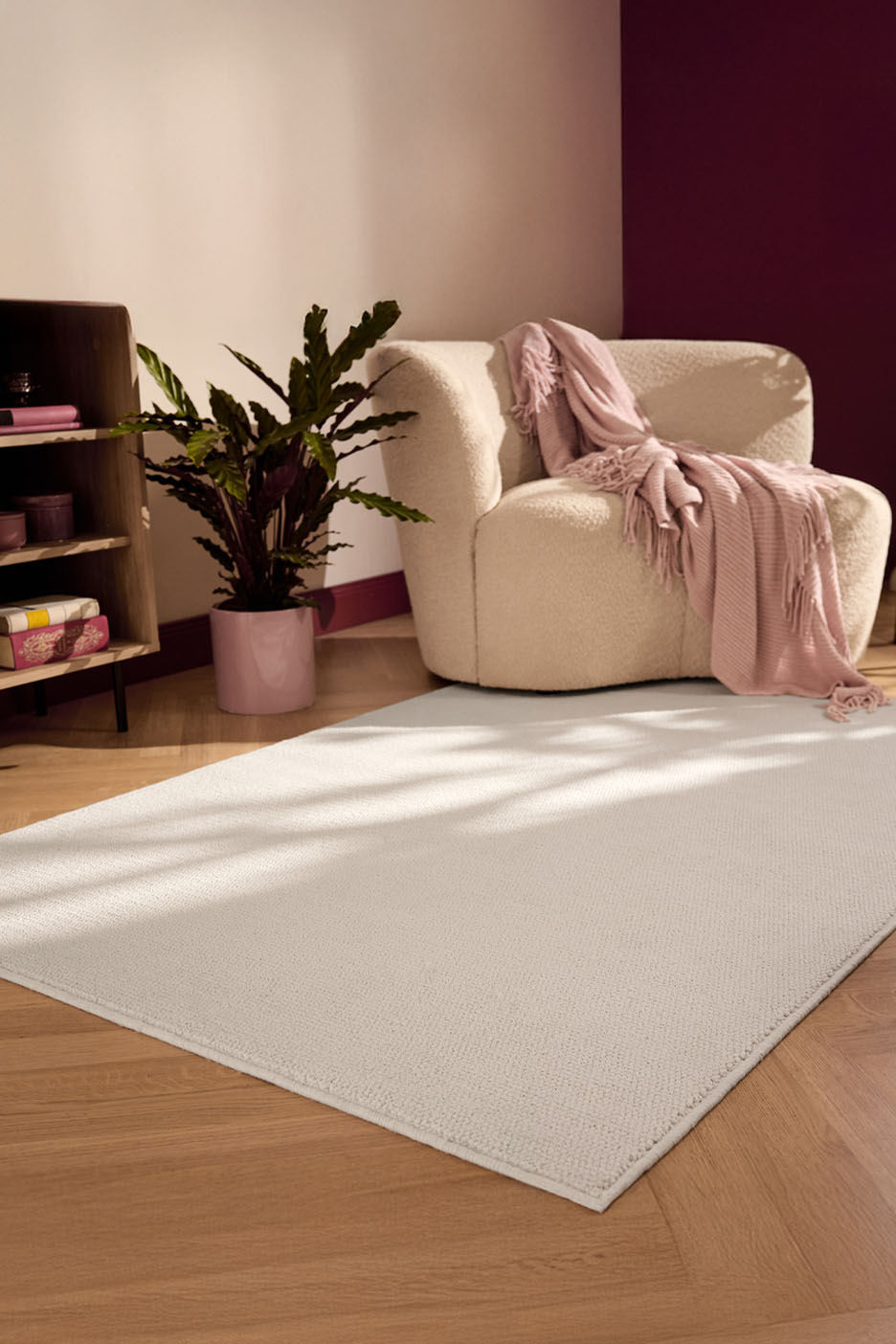 Un tapis beige clair posé sur un parquet clair, devant un fauteuil moelleux recouvert d'un plaid rose pâle.