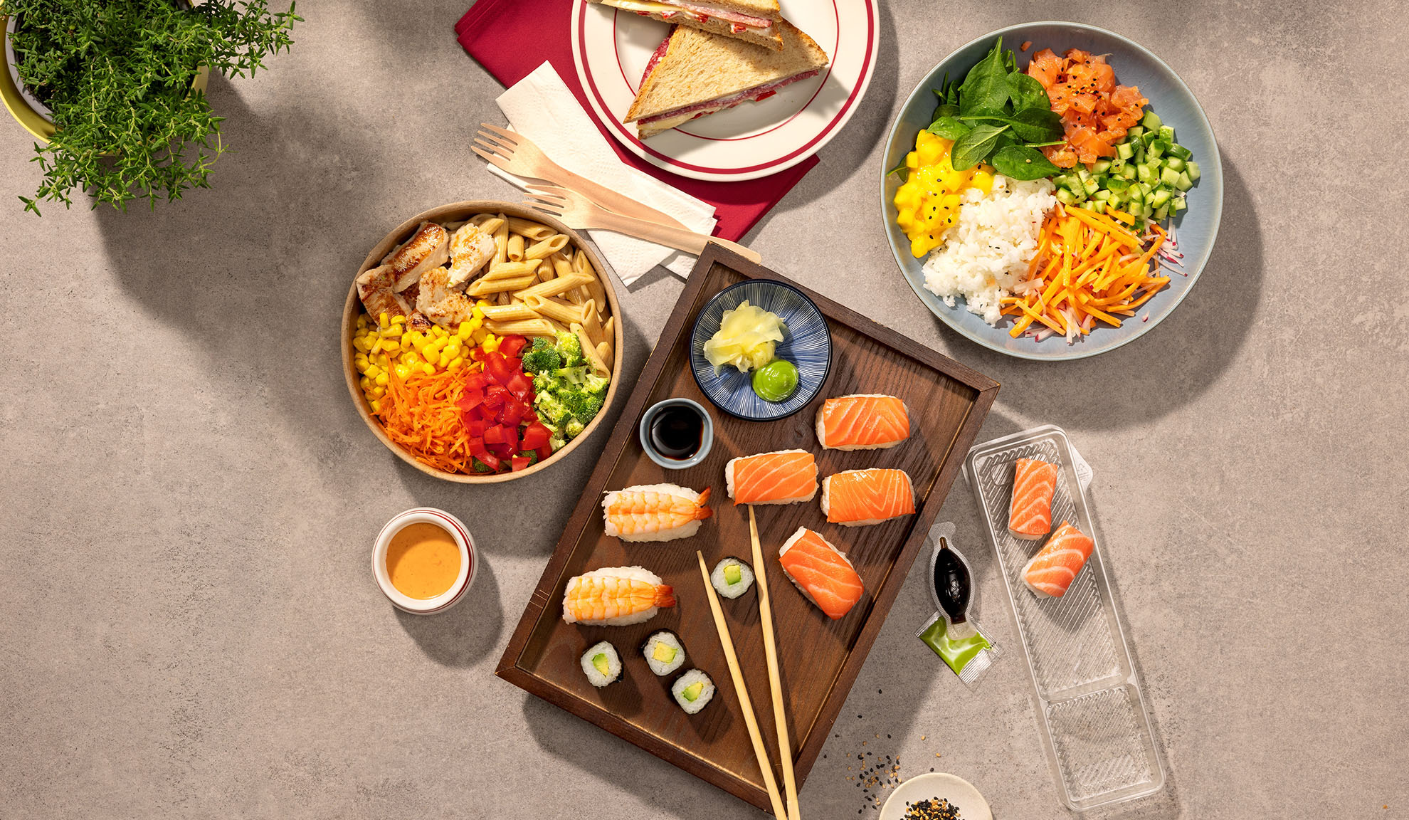 Vue de dessus de divers plats à emporter : sushis, poke bowl, salade de pâtes et sandwichs.