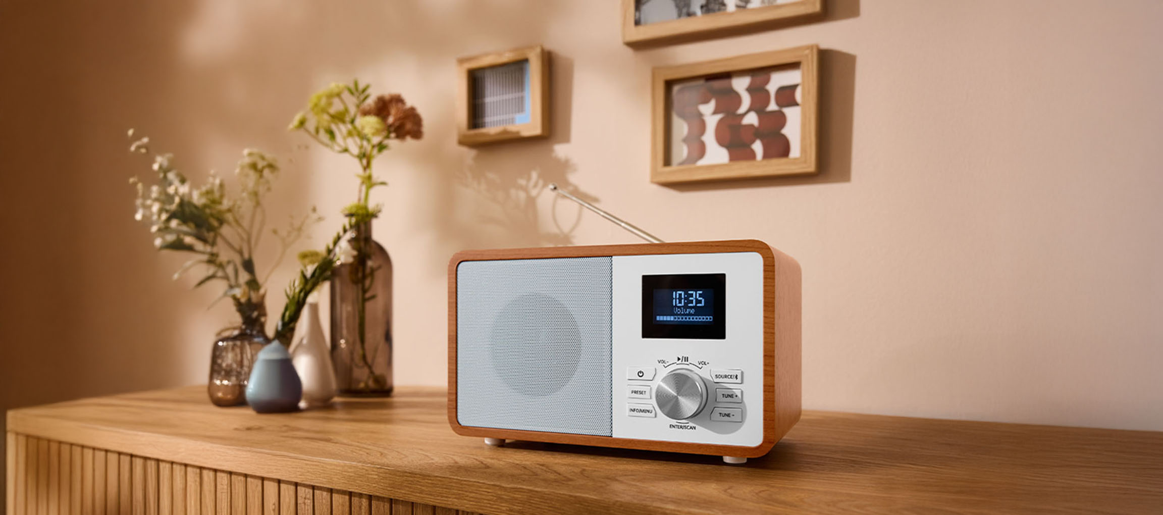 Une radio numérique en bois sur une commode, avec des vases et des tableaux au mur.