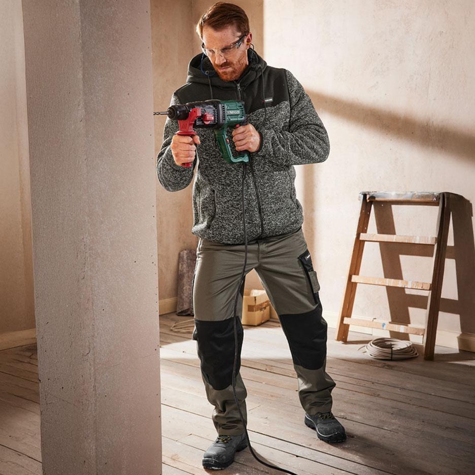 Homme en tenue de travail avec lunettes de sécurité perçant un mur avec un marteau perforateur.
