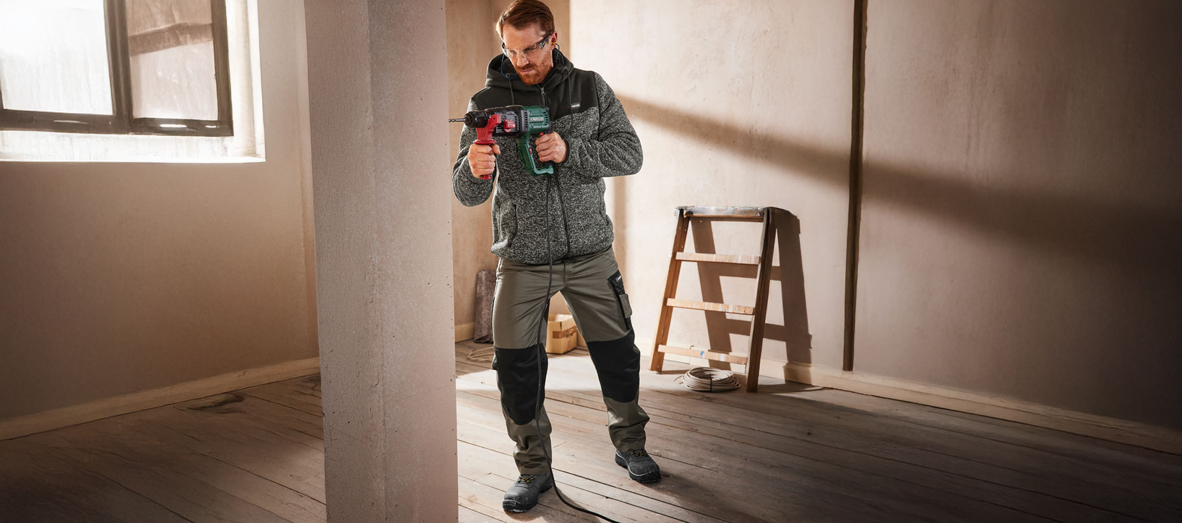 Homme en tenue de travail perçant un mur avec une perceuse.
