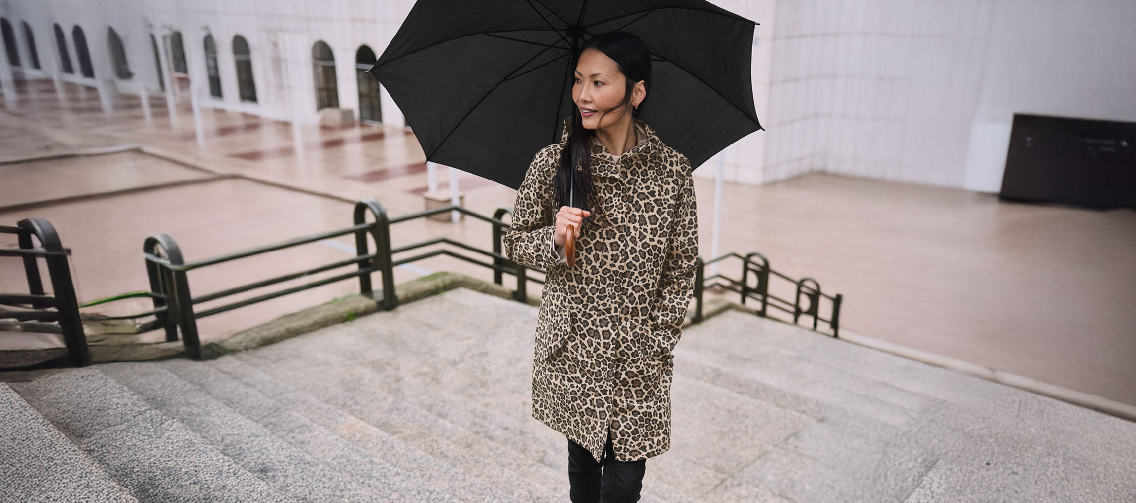 Femme en manteau léopard avec parapluie dans les escaliers.