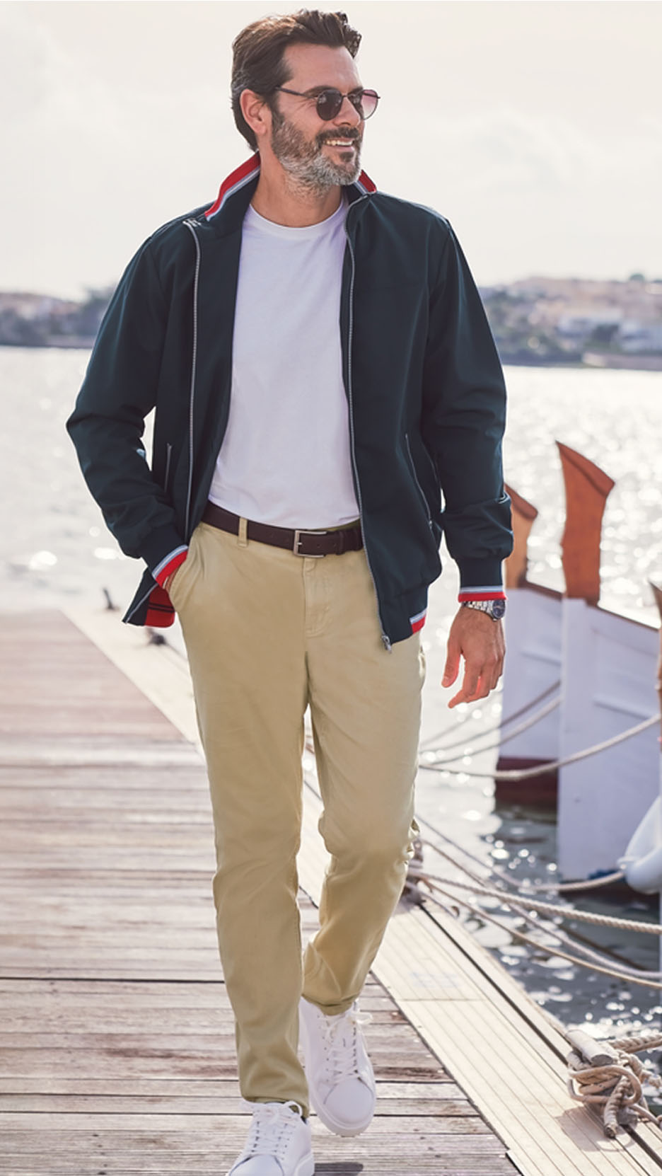 Homme en blouson aviateur, t-shirt blanc, pantalon chino et baskets blanches sur un quai.