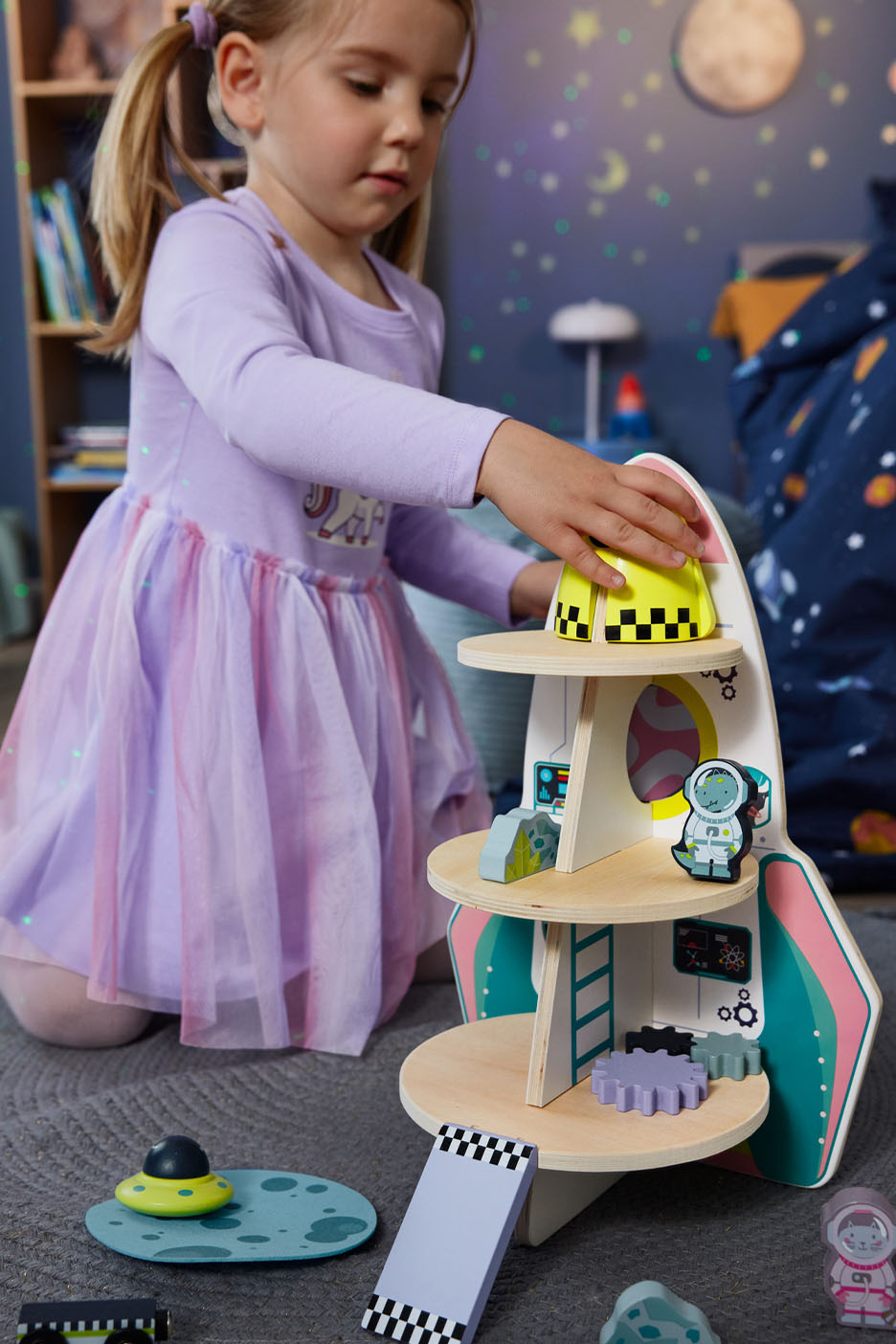 Jeune fille jouant avec une fusée spatiale en bois et accessoires.