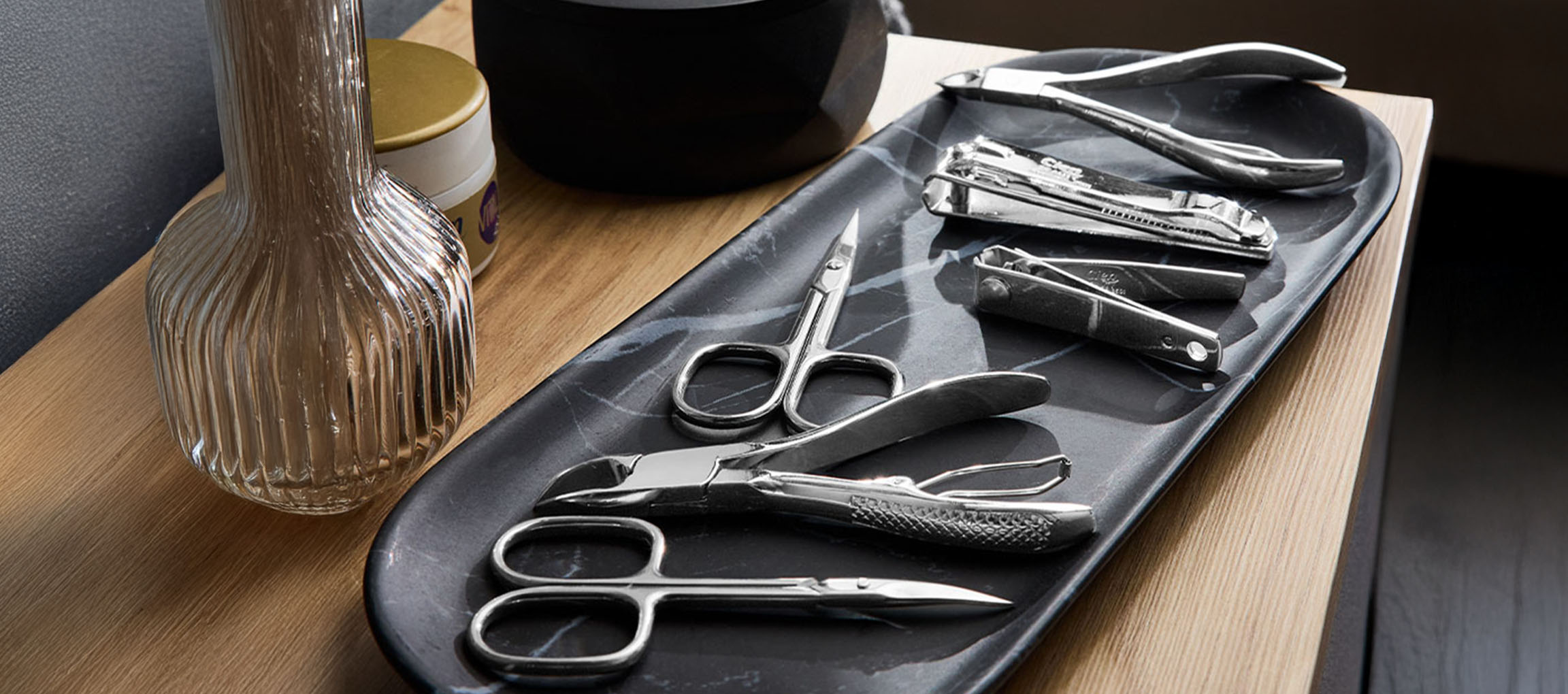Outils de manucure et pédicure sur un plateau en marbre, avec un vase et un pot en arrière-plan.