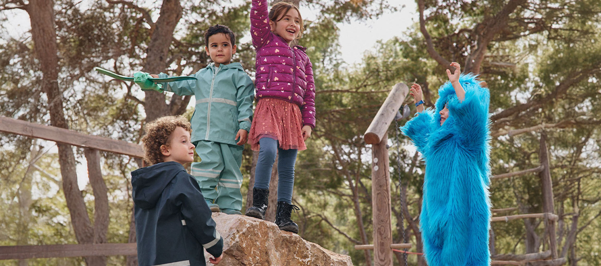 Quatre enfants jouent dehors, deux en vêtements d'extérieur, un en costume de monstre bleu.
