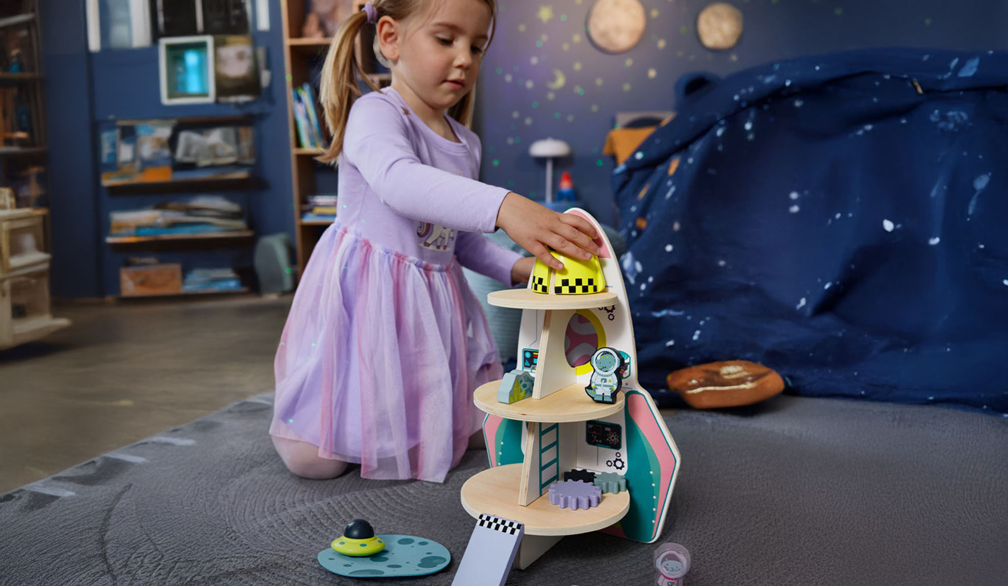 Une fille joue avec une fusée jouet et des accessoires spatiaux dans une chambre à thème.
