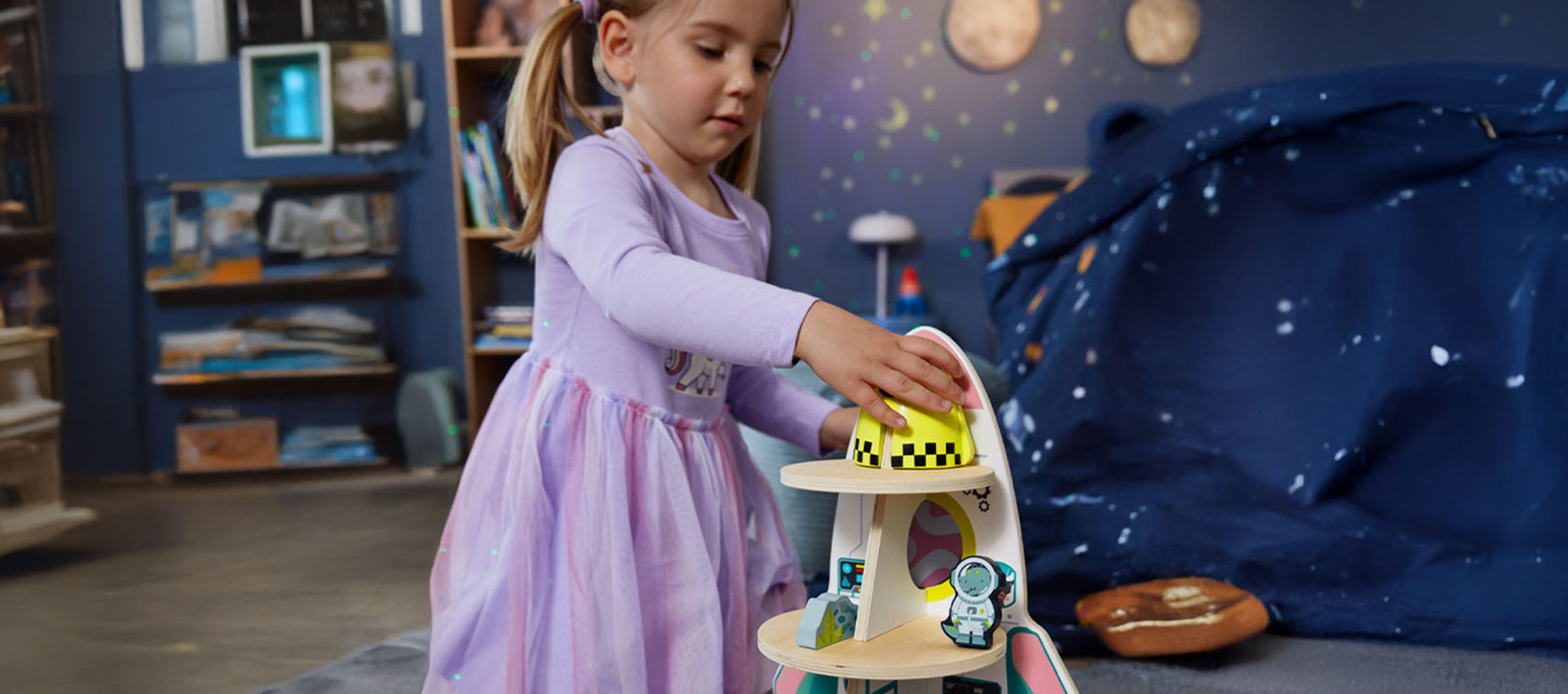 Petite fille jouant avec un jouet de vaisseau spatial dans une chambre sur le thème de l'espace.