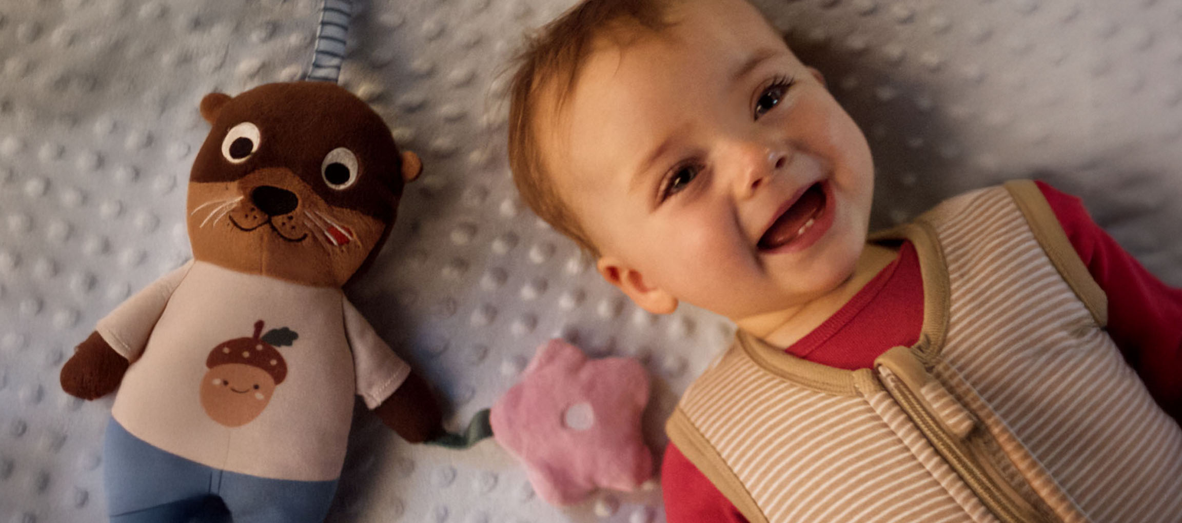 Bébé souriant et une peluche avec un gland sur le ventre.