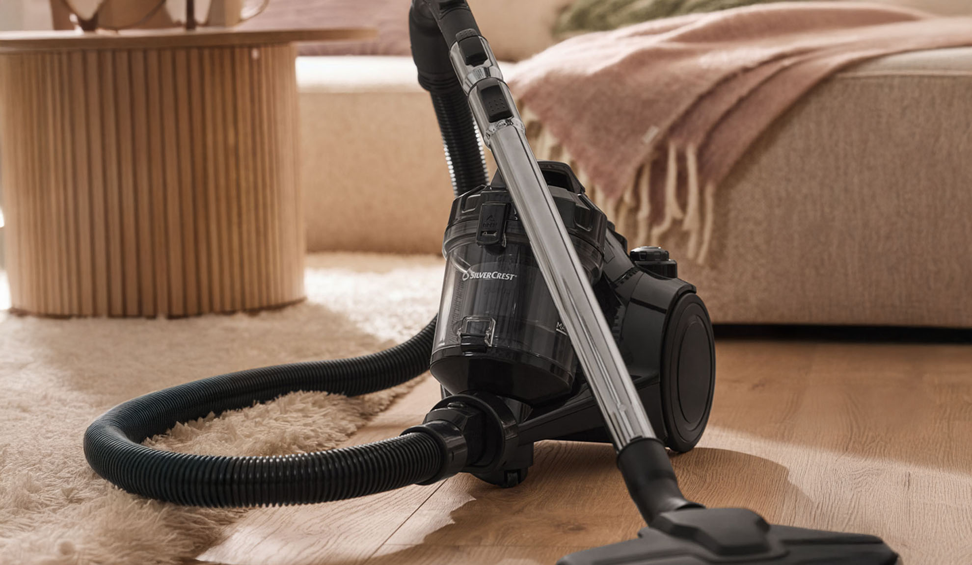 Aspirateur noir sur un parquet, avec un tapis moelleux et des meubles en arrière-plan.