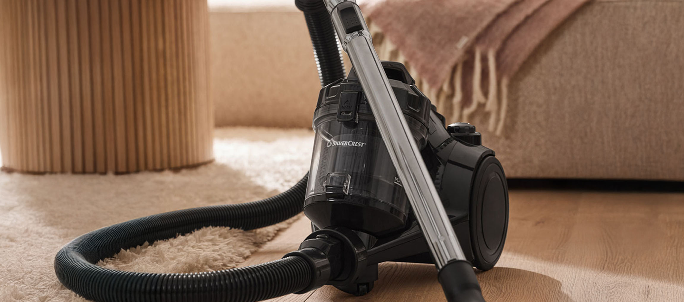 Un aspirateur SilverCrest noir sur un tapis et un parquet.