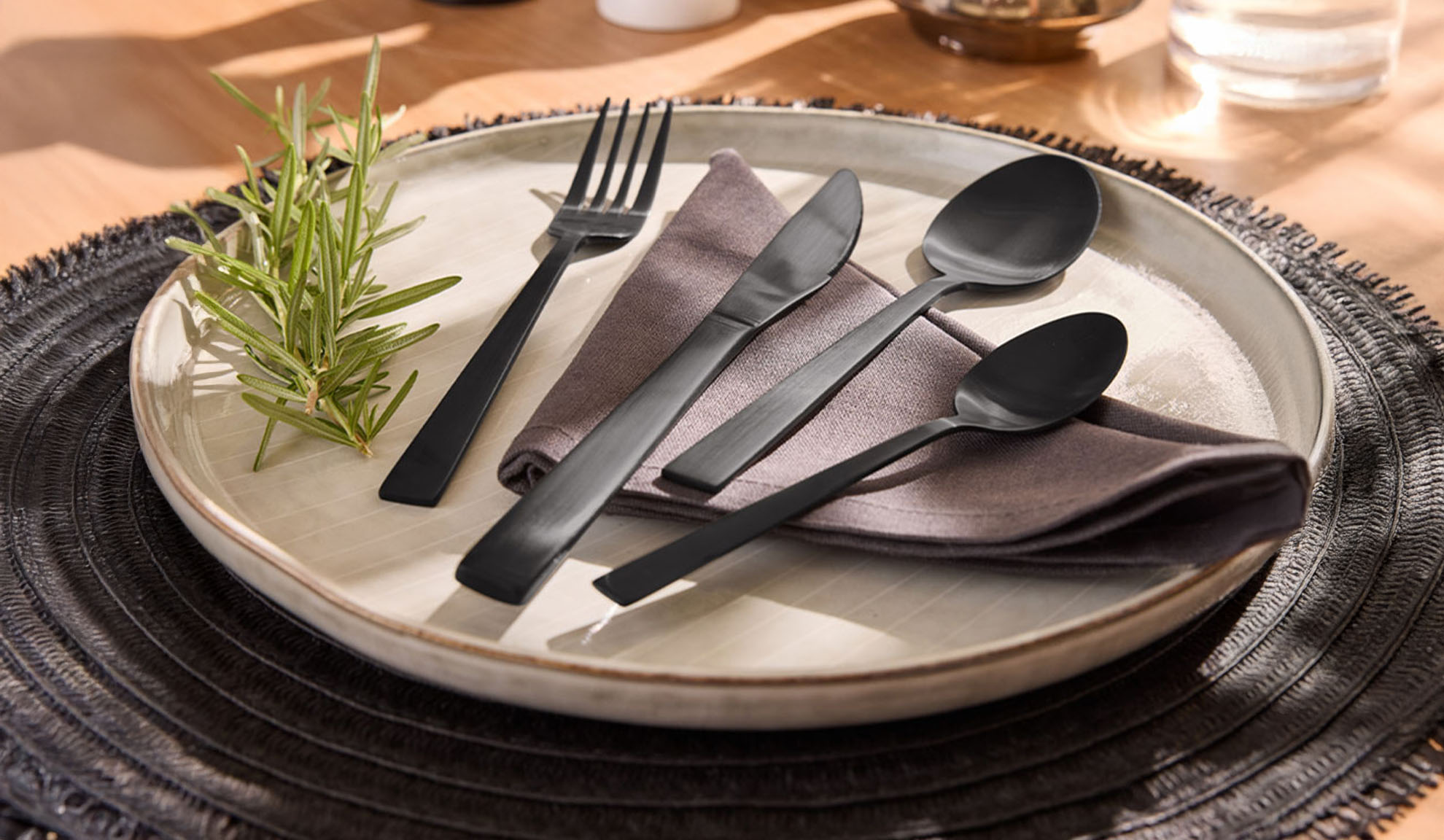 Ensemble de couverts noirs avec assiette, serviette et brin de romarin sur un set.