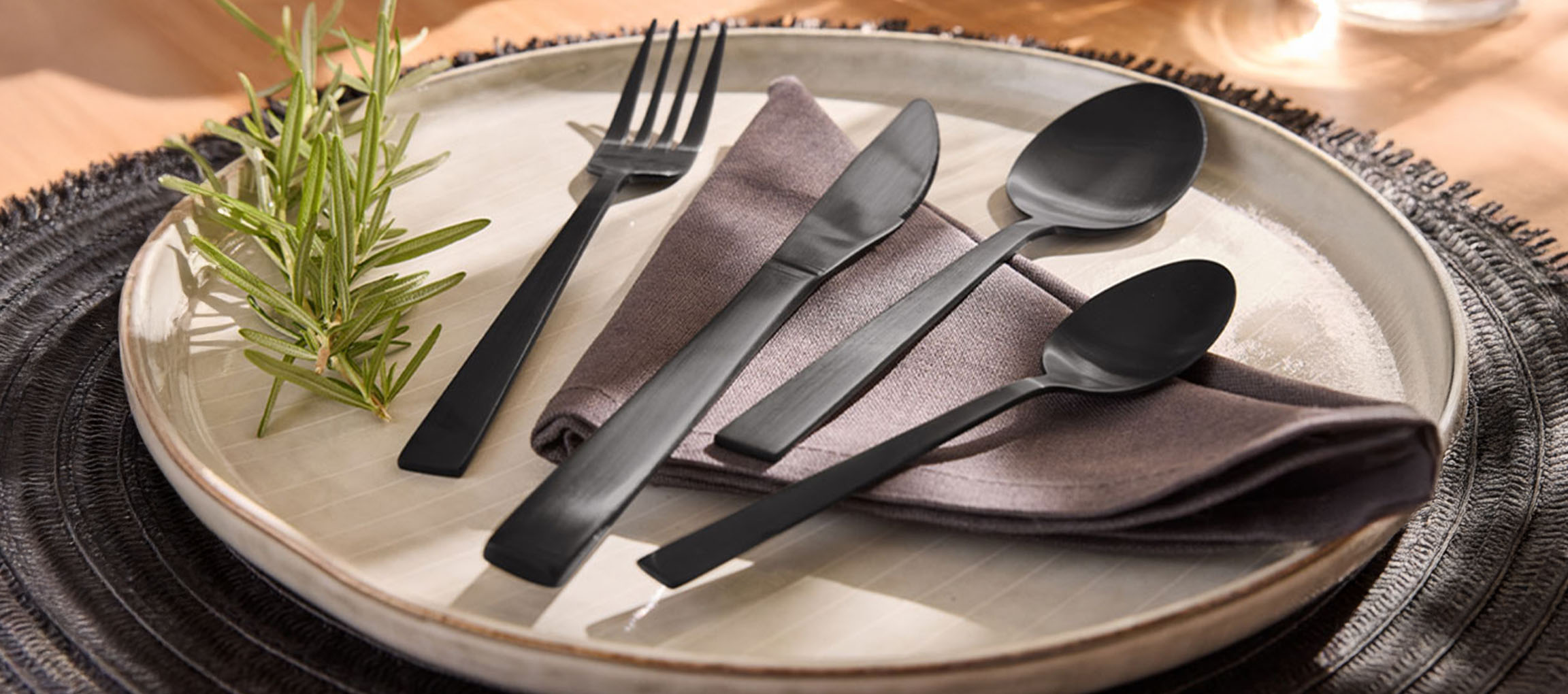 Couverts noirs mats, assiette et serviette sur une table en bois.