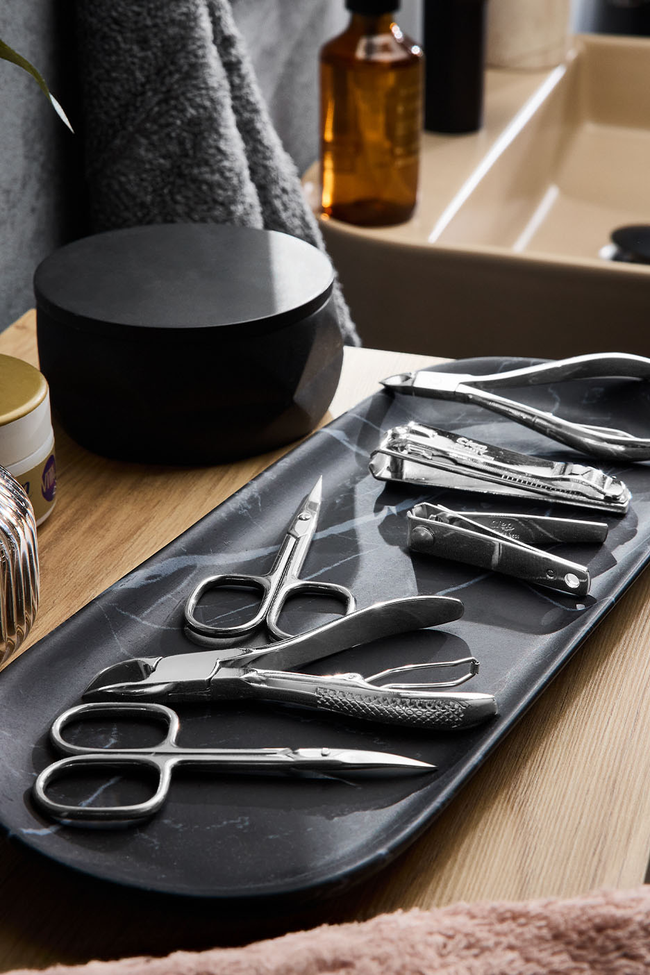 Ensemble d'outils de manucure et pédicure sur un plateau en marbre, près d'un lavabo.