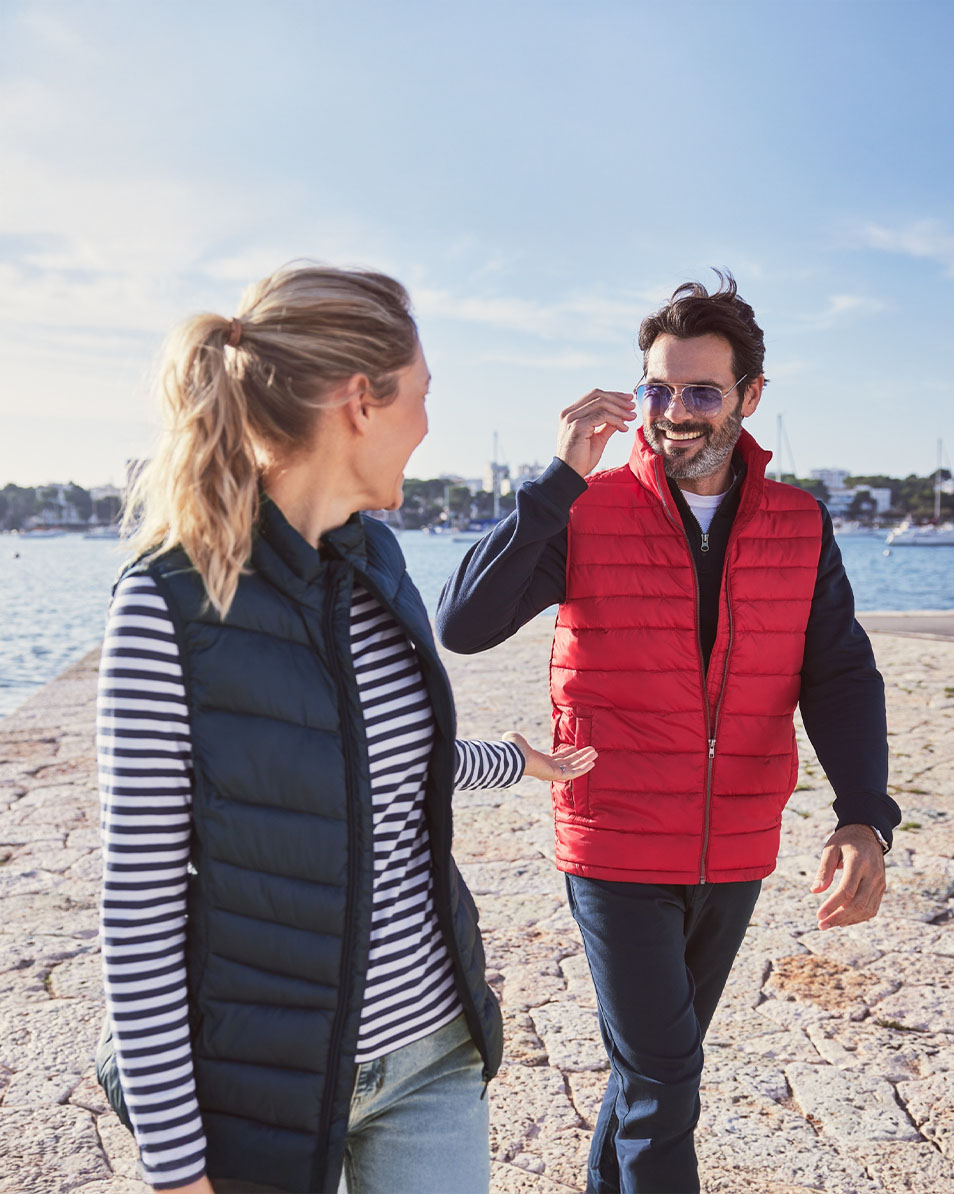 Un couple souriant porte des gilets matelassés sur un quai ensoleillé.