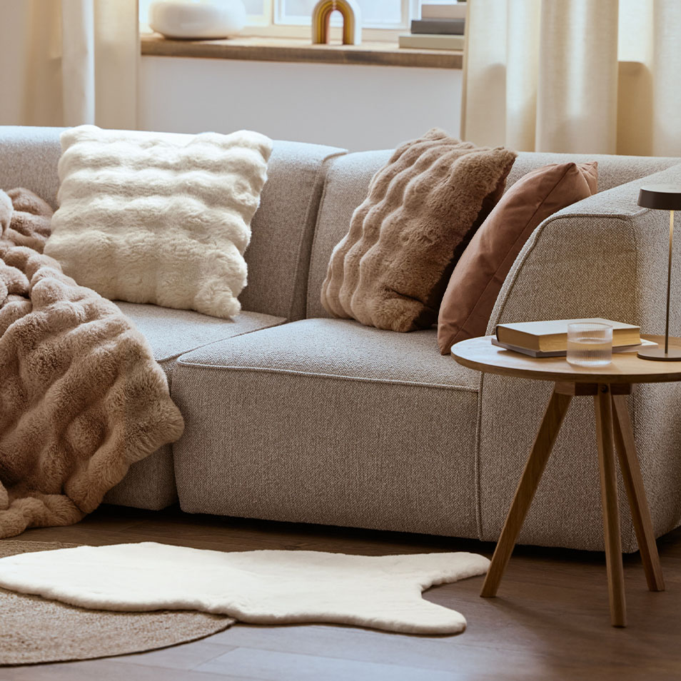 Canapé modulaire gris avec coussins et plaids moelleux, à côté d'une table basse.