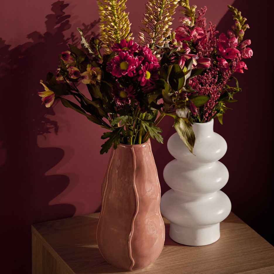 Deux vases avec des fleurs sur une table en bois devant un mur rouge foncé.