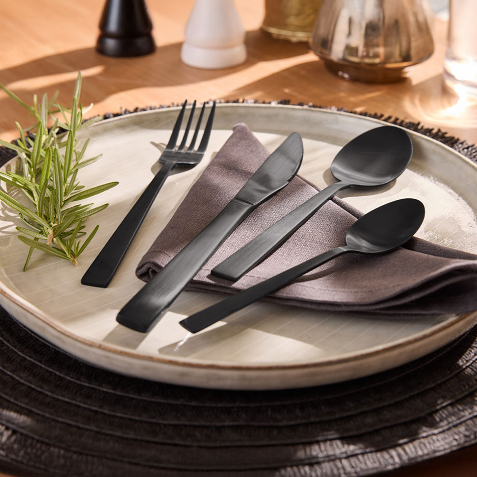 Ensemble de couverts noirs avec une fourchette, un couteau et deux cuillères sur une assiette avec du romarin.