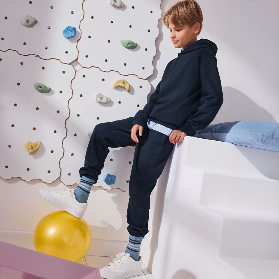 Un garçon porte un sweat à capuche et un pantalon de survêtement bleu marine, avec un mur d'escalade en arrière-plan.