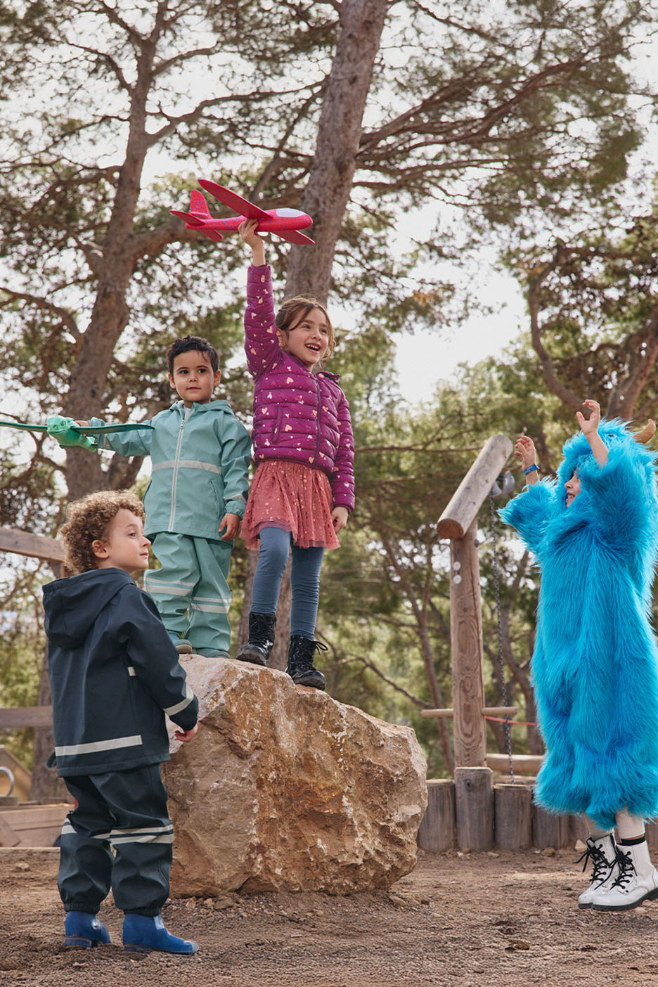Des enfants en vêtements d'extérieur colorés jouent dehors, un enfant en costume de monstre bleu.