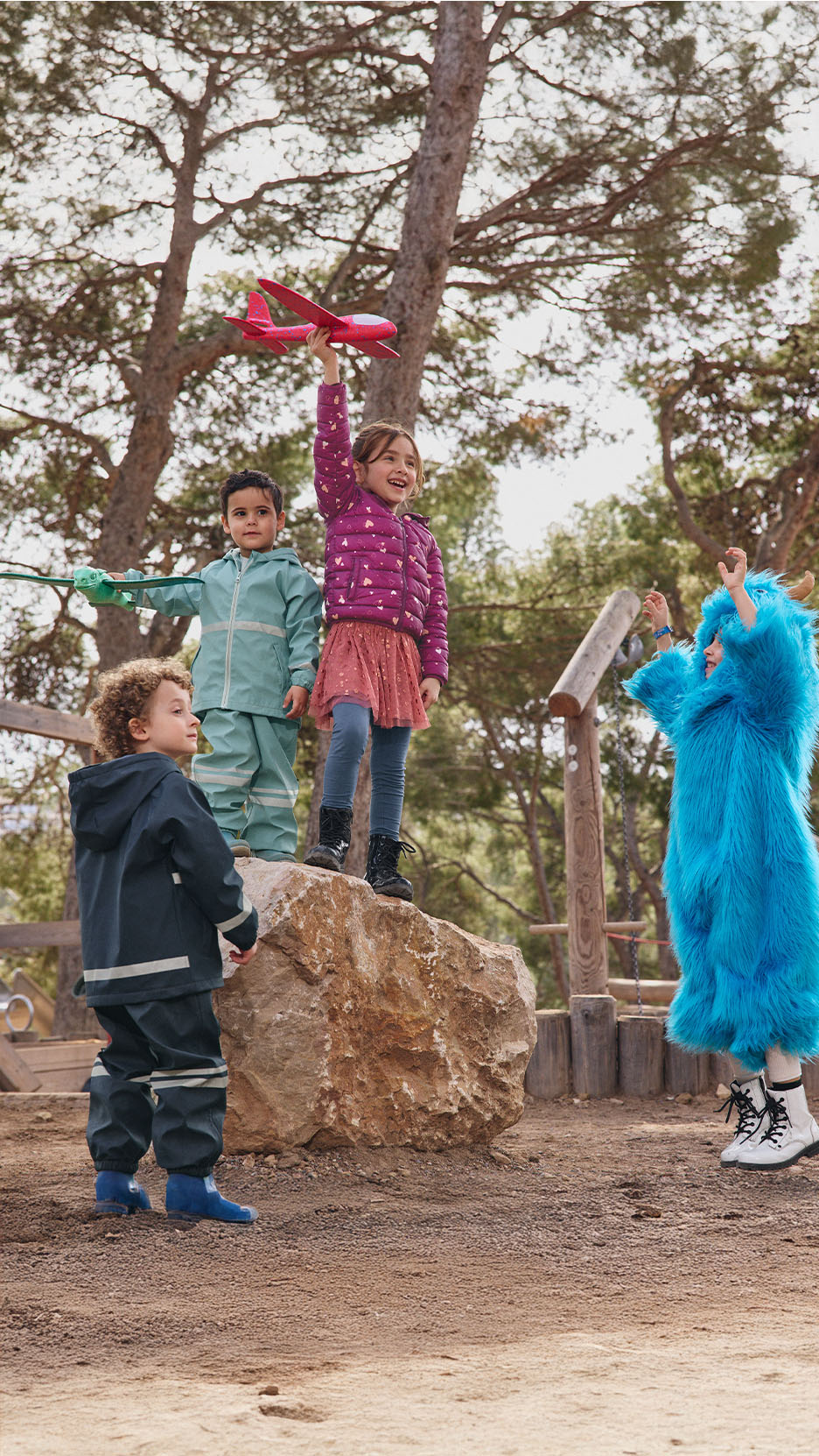Des enfants en vêtements d'extérieur jouent dans un parc, un enfant en costume de monstre bleu.
