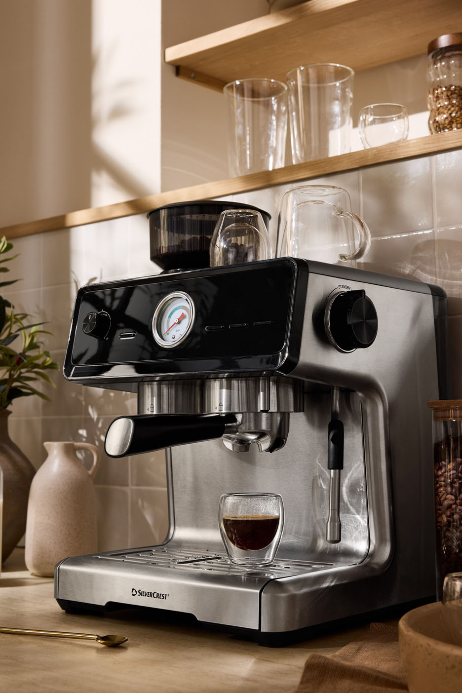 Une machine à expresso Silvercrest avec une tasse de café et des verres sur une étagère.