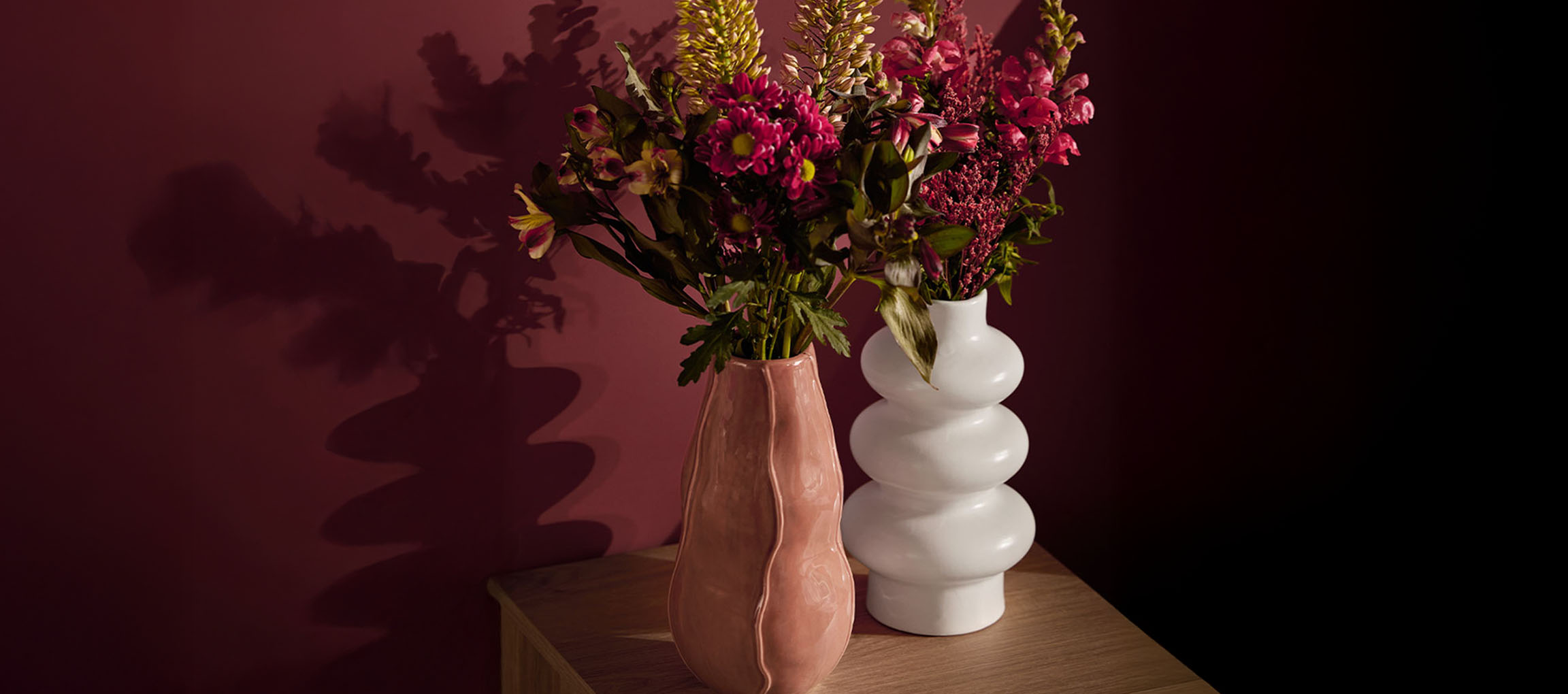 Deux vases avec des fleurs, un rose et un blanc, sur une surface en bois.