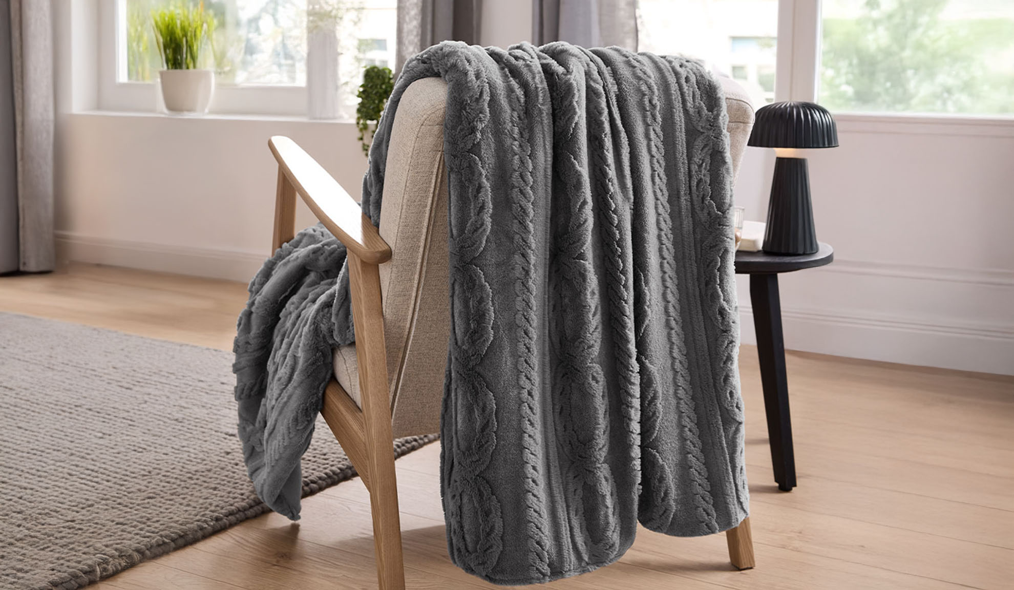 Un plaid gris en tricot torsadé drapé sur un fauteuil en bois clair dans un salon.