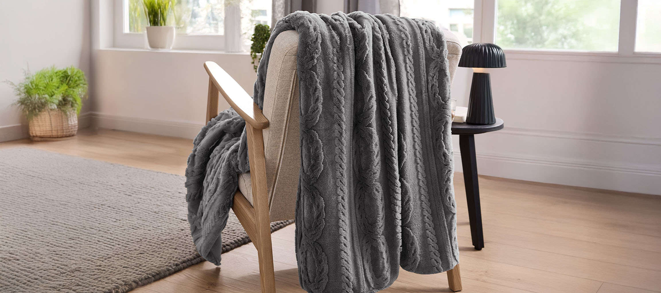 Plaid gris en tricot torsadé drapé sur un fauteuil en bois clair dans une pièce lumineuse.