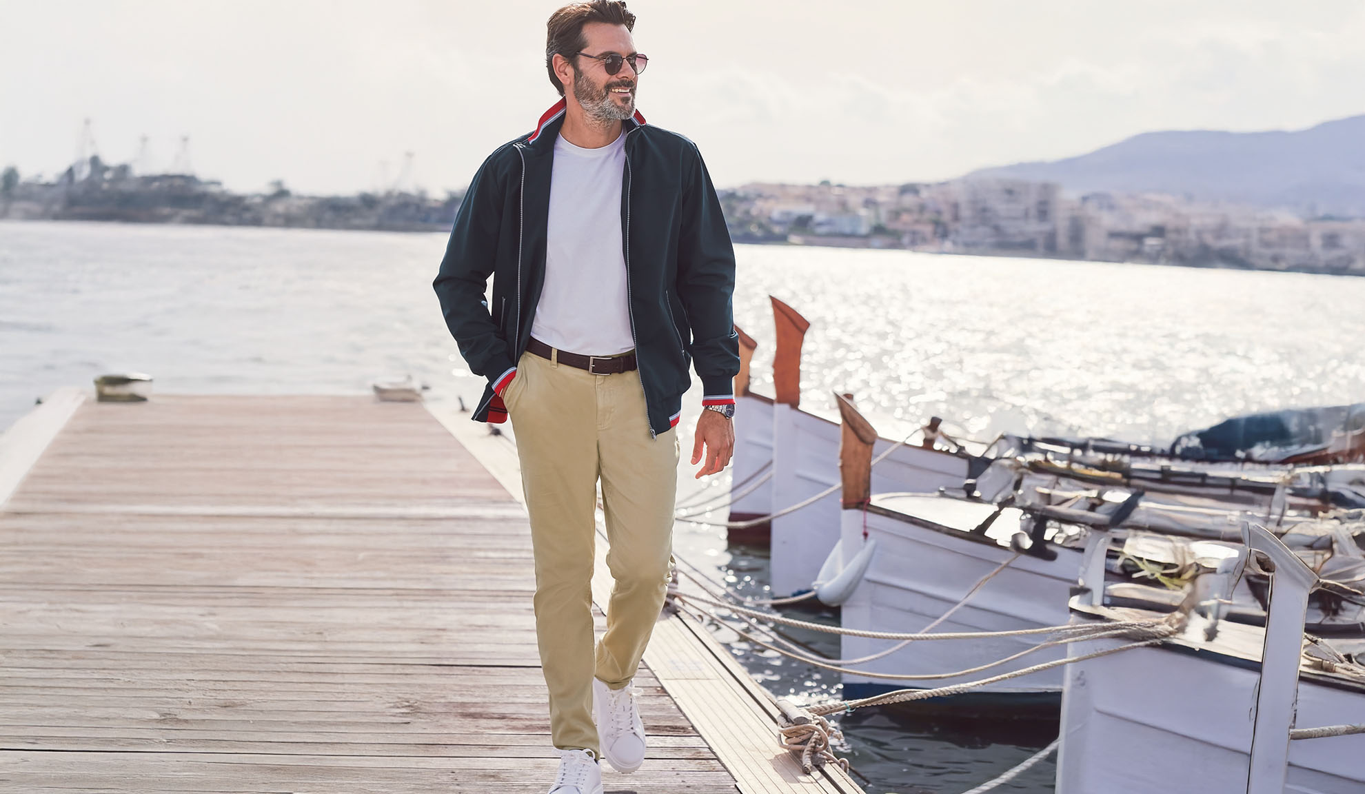 Homme en veste bleu marine, t-shirt blanc et pantalon kaki sur une jetée.