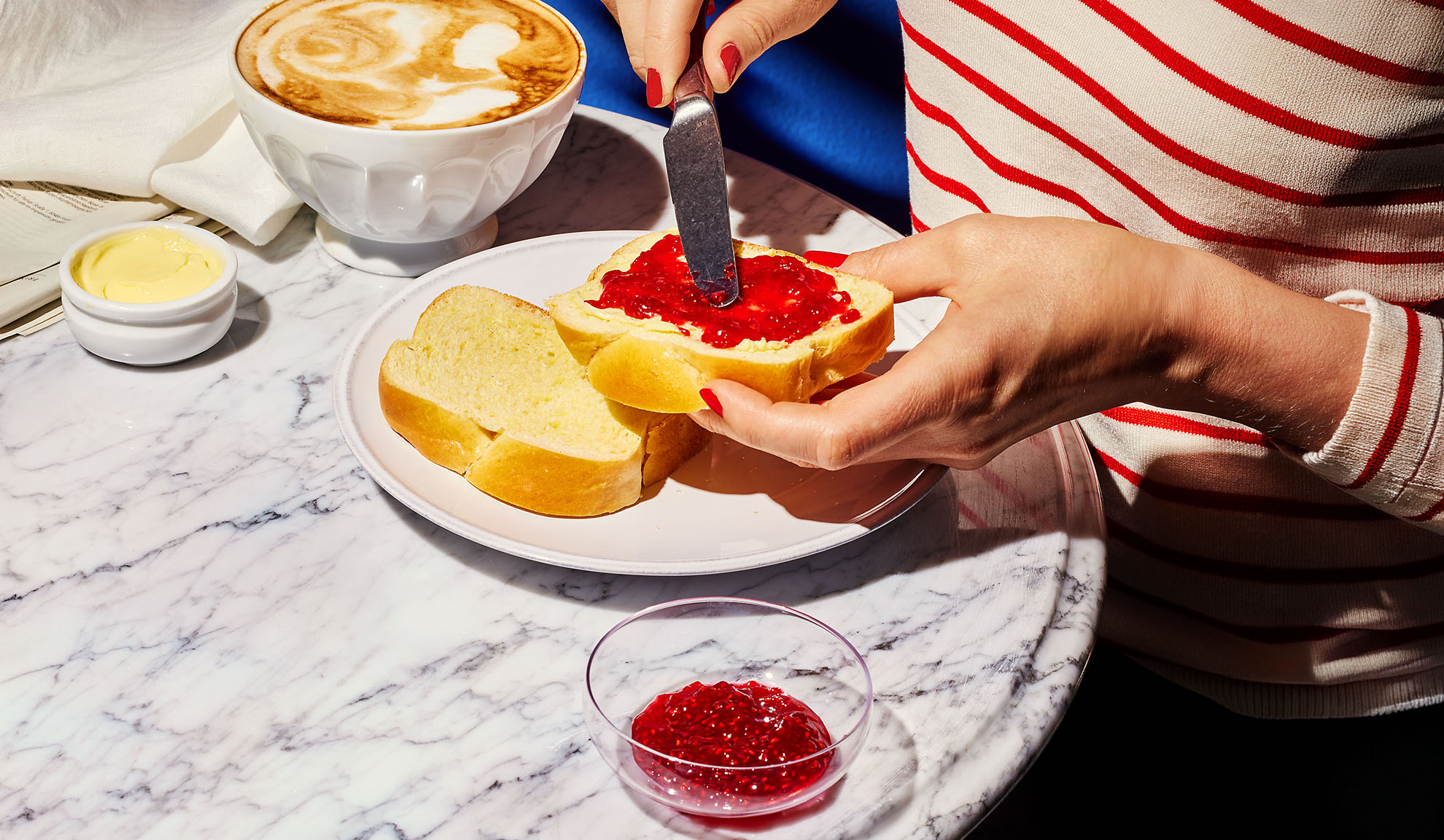Mains étalant de la confiture sur du pain brioché, avec café et beurre sur table en marbre.