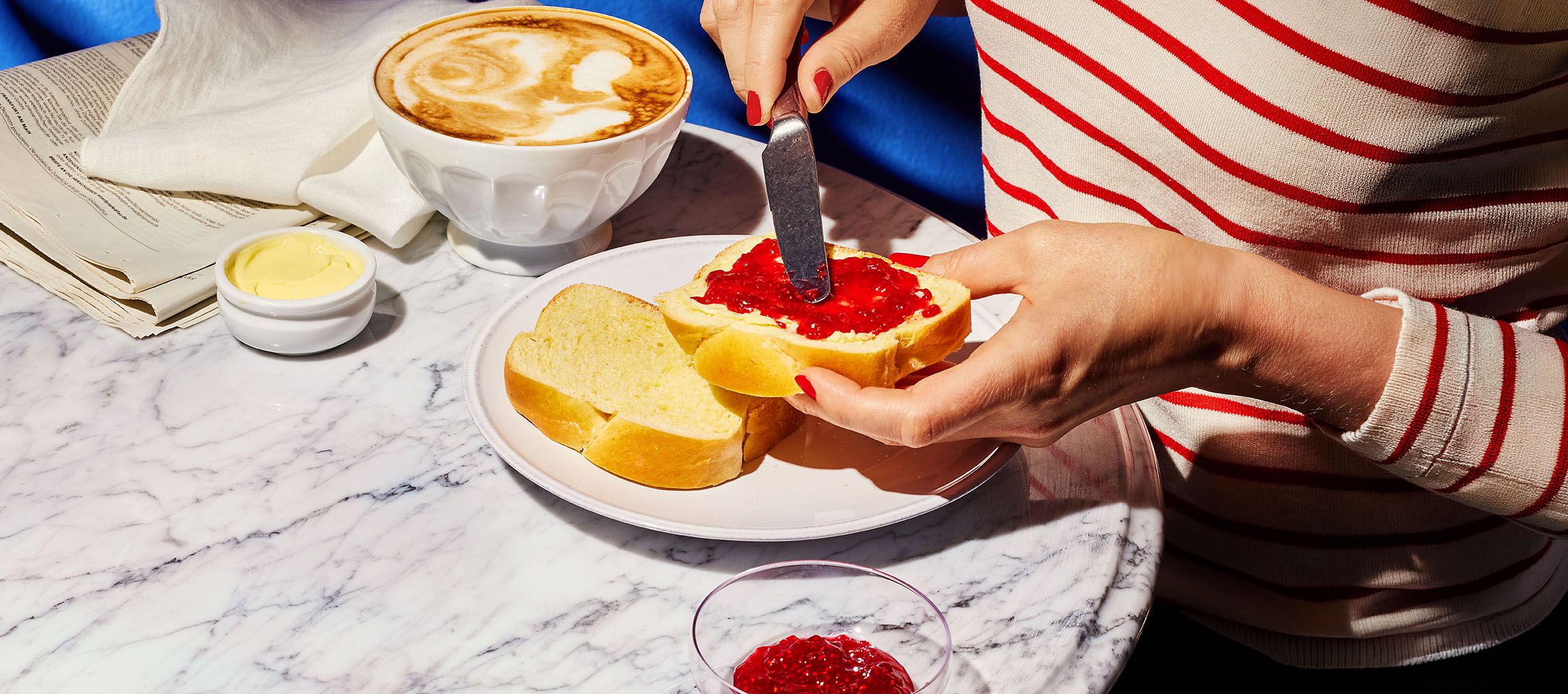 Mains étalant de la confiture sur du pain brioché, avec café et beurre sur table en marbre.