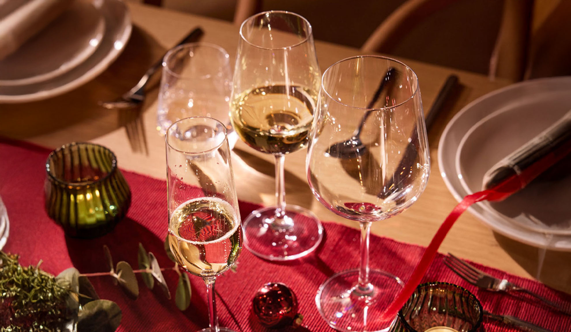 Table de fête dressée avec verres à vin, flûte à champagne et décorations de Noël.