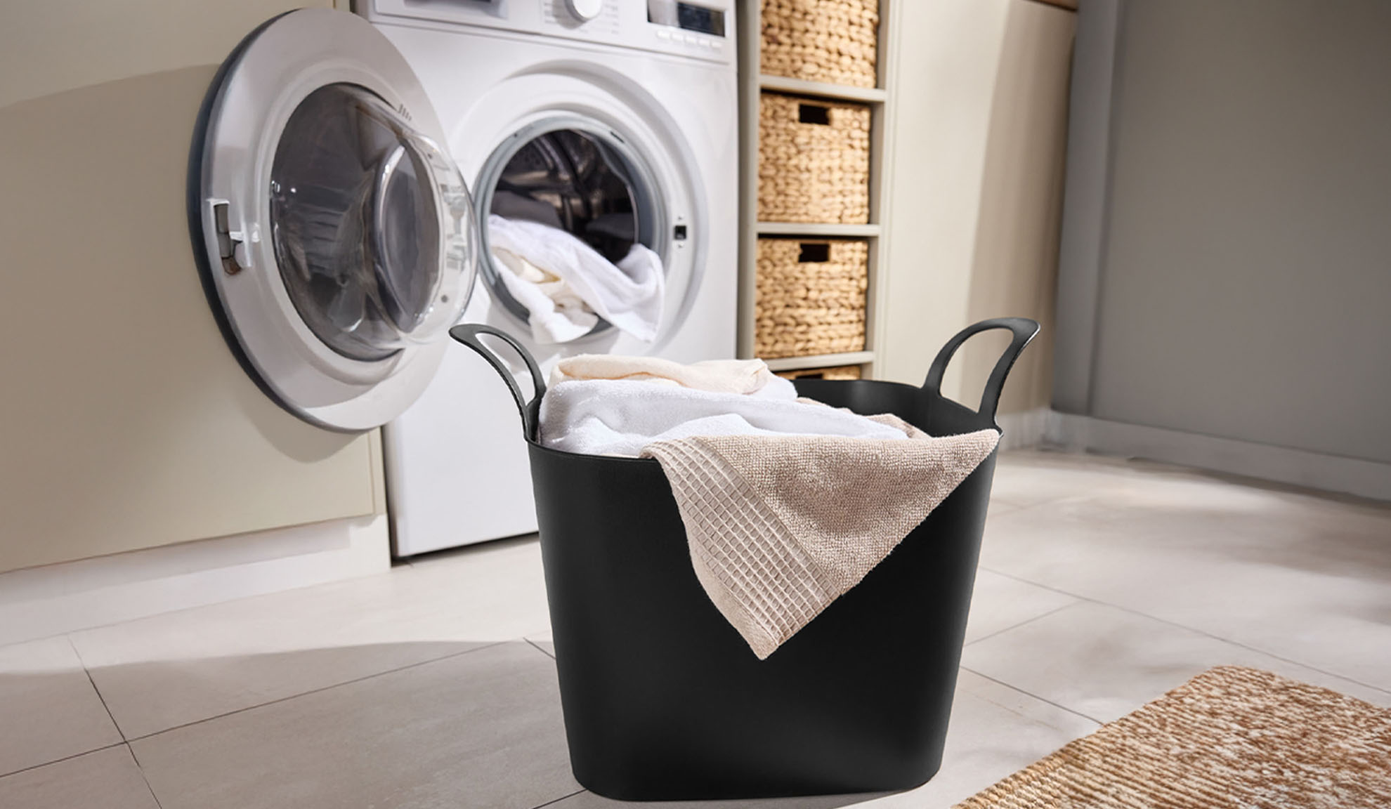 Lave-linge avec porte ouverte et panier à linge noir rempli de serviettes