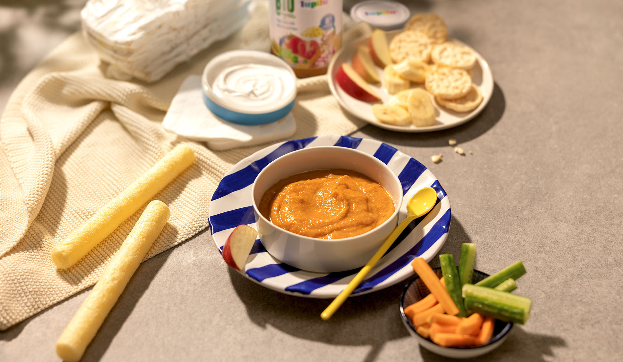 Aliments pour bébés, yaourt, fruits et légumes coupés, craquelins et collations sur une table.