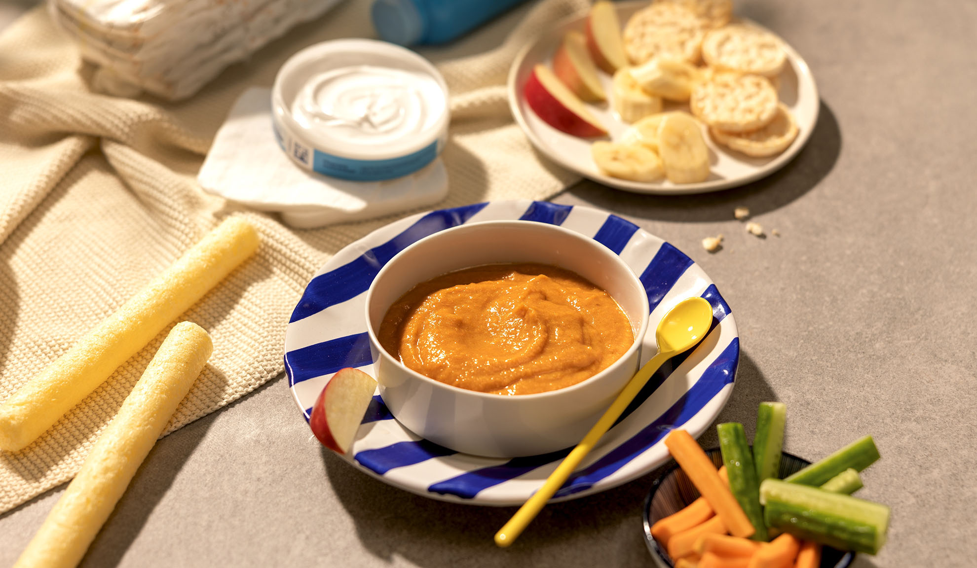 Repas bébé : bol de purée, fruits, bâtonnets et légumes sur la table.