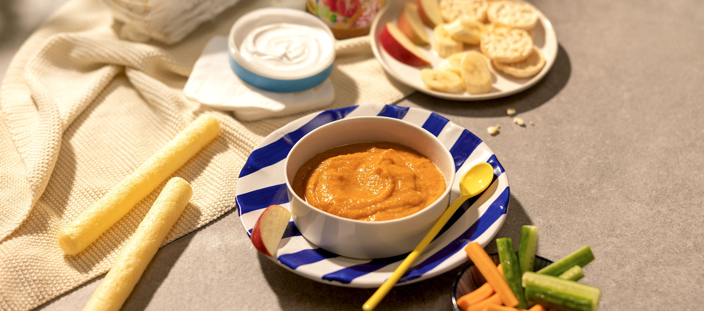 Aliments pour bébé: bol de purée de carottes, bâtonnets de maïs, yaourt, fruits et légumes.
