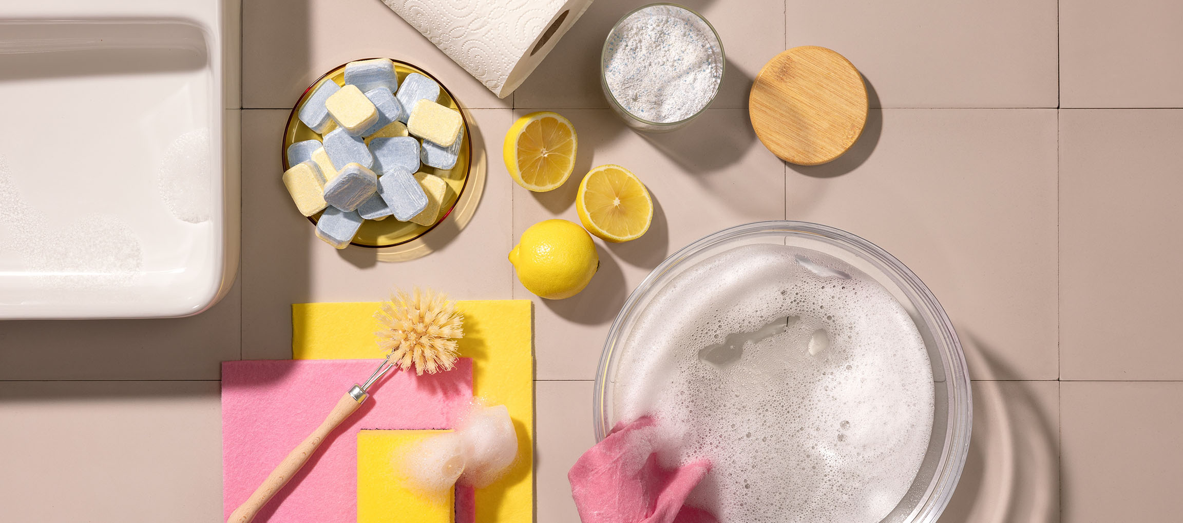 Produits de nettoyage : tablettes lave-vaisselle, citrons, poudre, brosse et chiffons.