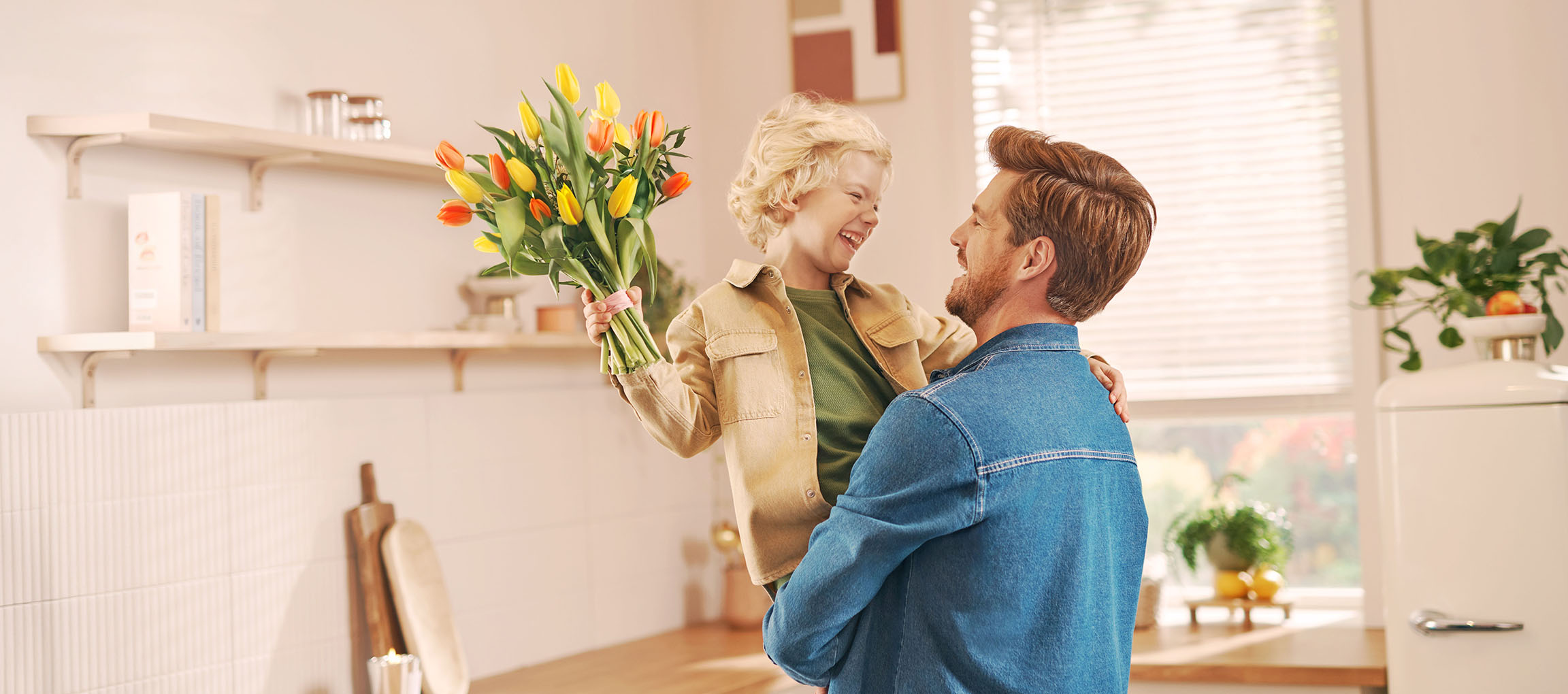 Un garçon tenant un bouquet de tulipes, riant avec un homme dans une cuisine.