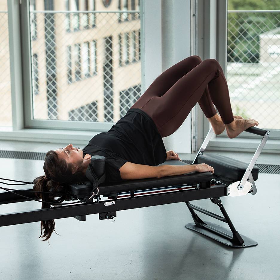 Femme faisant du Pilates sur un appareil reformer, jambes levées.