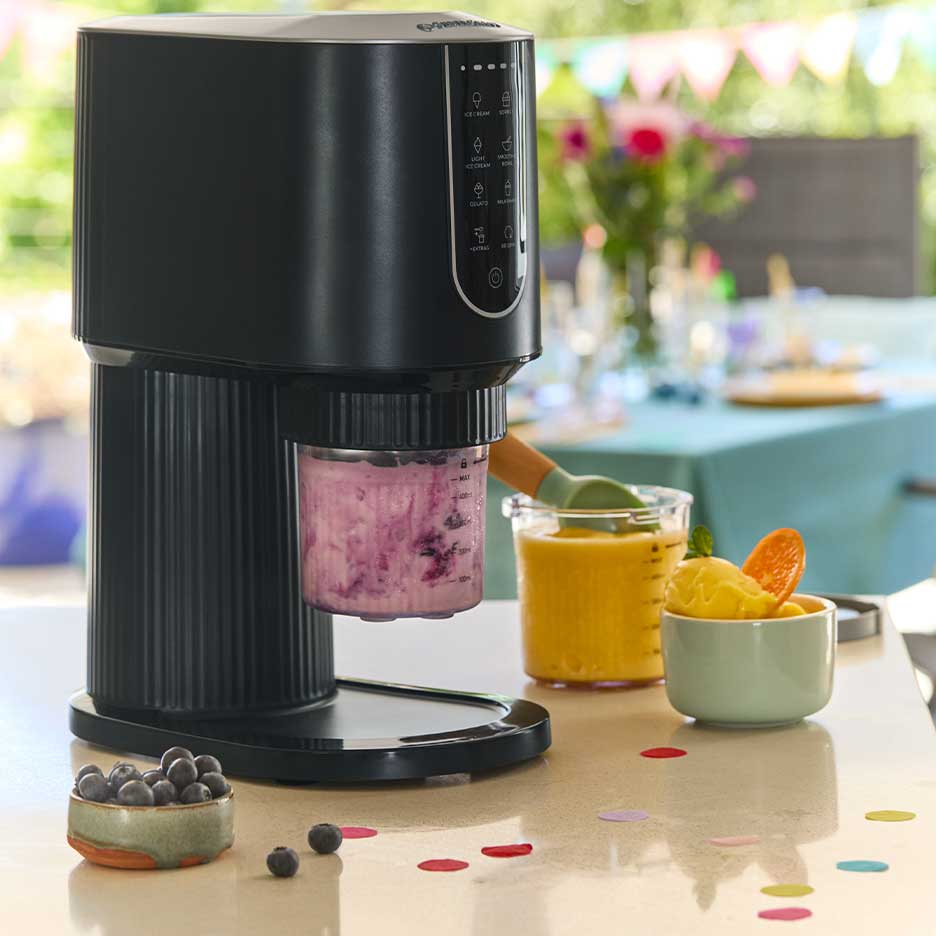 Machine à glace noire avec glace violette, entourée de glace à la mangue et de myrtilles.