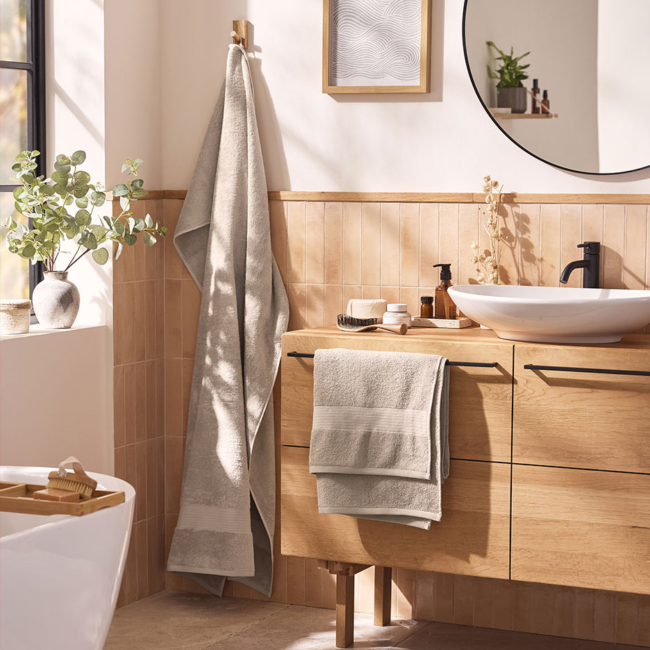 Salle de bain moderne avec serviettes beiges, lavabo blanc et meubles en bois.