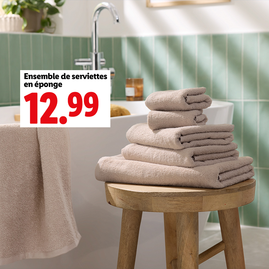 Un ensemble de serviettes en éponge beige est présenté dans une salle de bain.