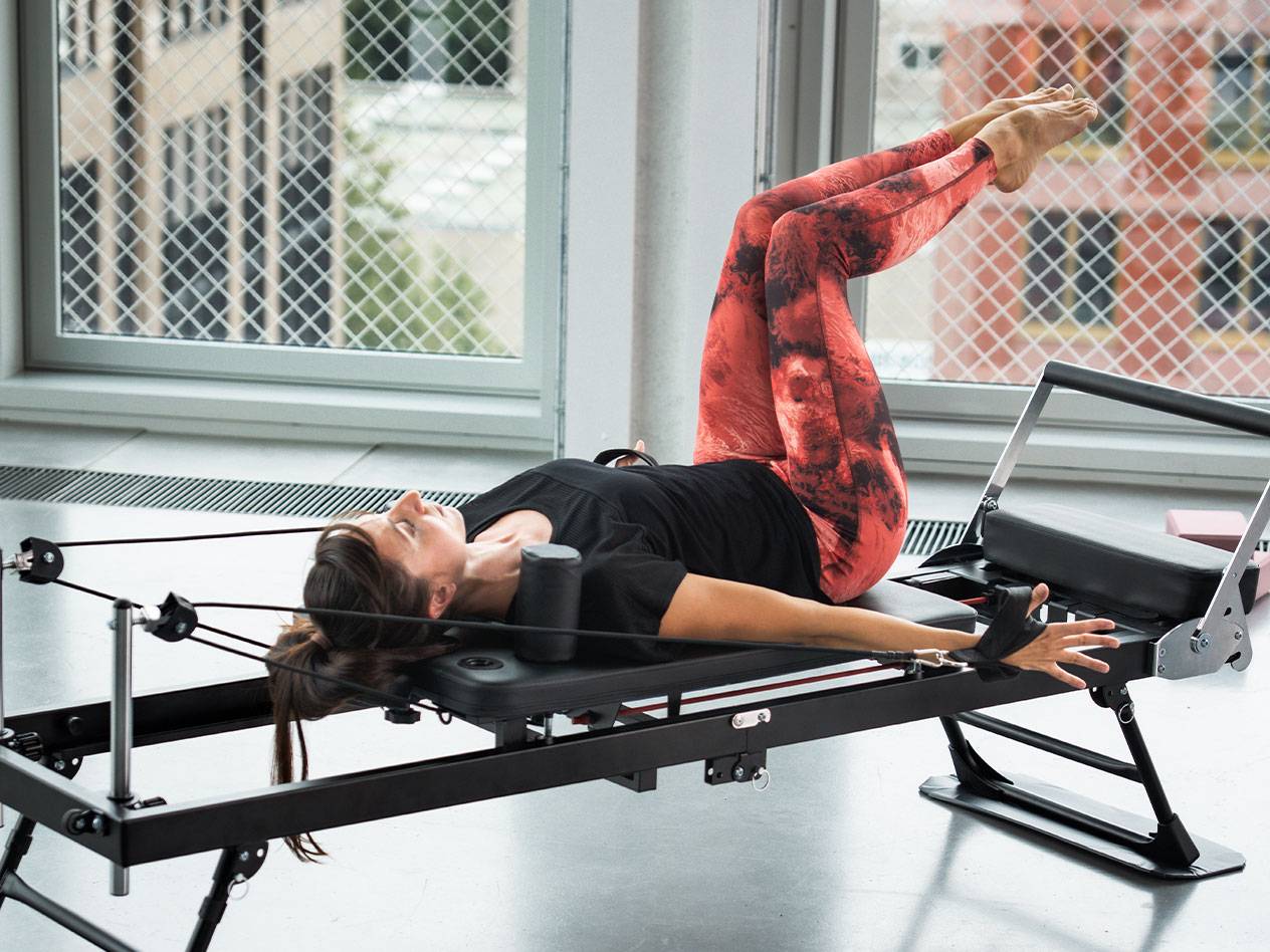 Femme faisant du Pilates sur un reformer, en leggings rouges et noirs