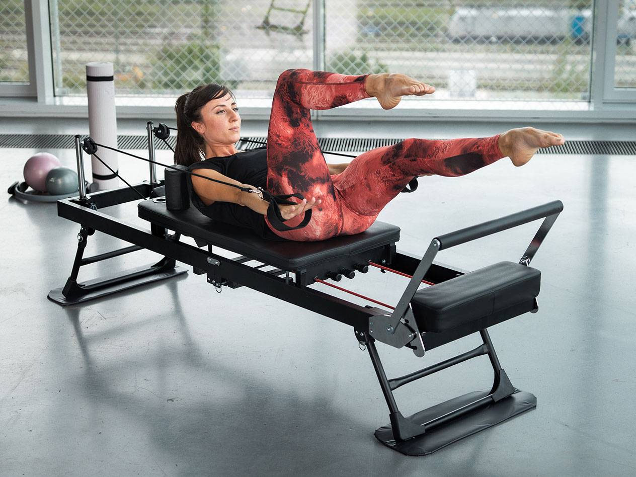 Femme faisant du Pilates sur un appareil de Pilates noir avec des détails rouges.