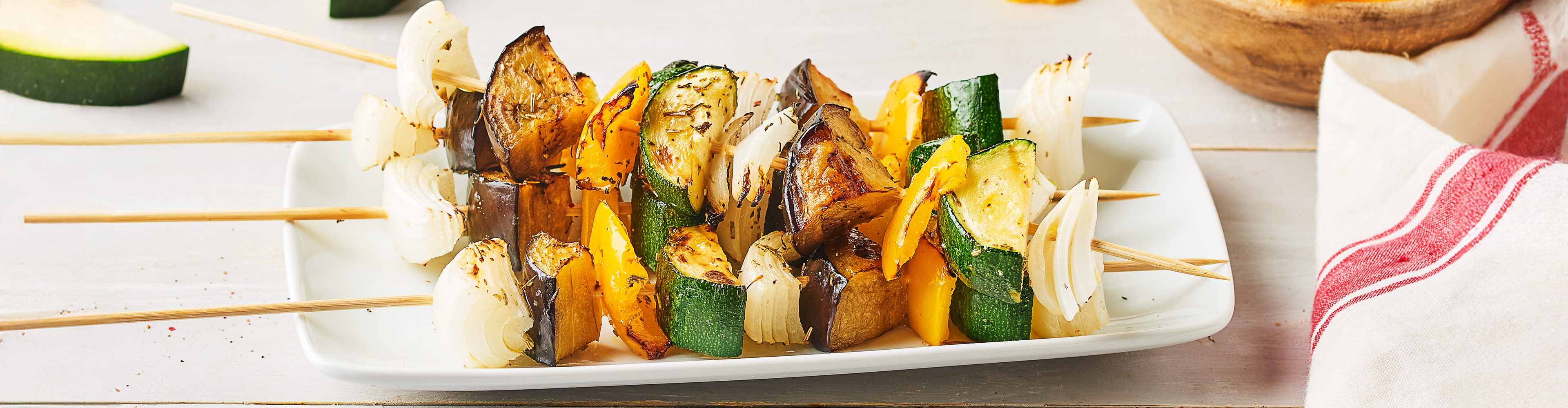 Brochettes de légumes grillés sur une assiette blanche.