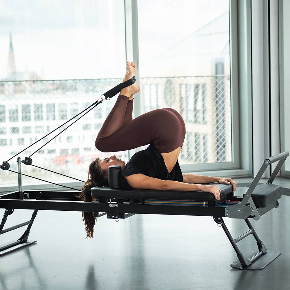 Femme faisant du Pilates sur un reformer, jambes levées et pieds dans des sangles.